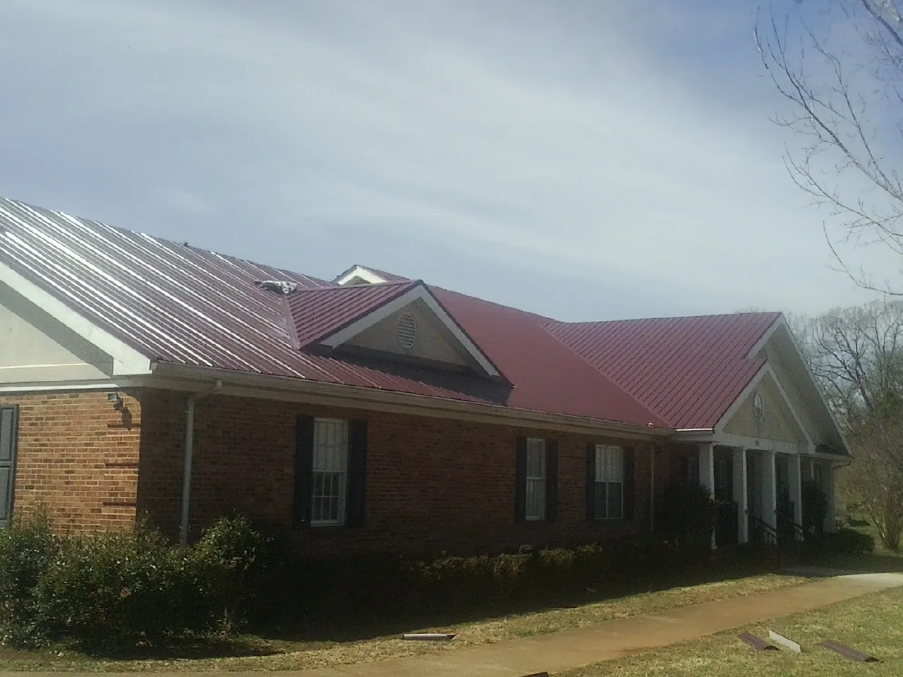 Red metal roof with gabled entries on a long brick building, from a Hail Damage Roof Repair job in Hollidaysburg