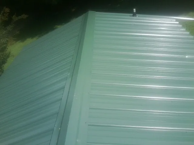 New green metal panels meeting at the ridge of a roof — Flat Roof Repair work by our crew in Hollidaysburg