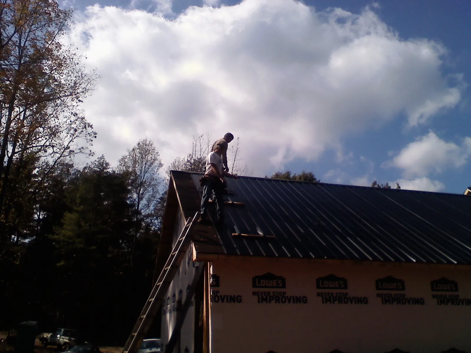 Roofer fastening dark metal panels high against a cloudy sky, from a Roof Inspection job in Hollidaysburg