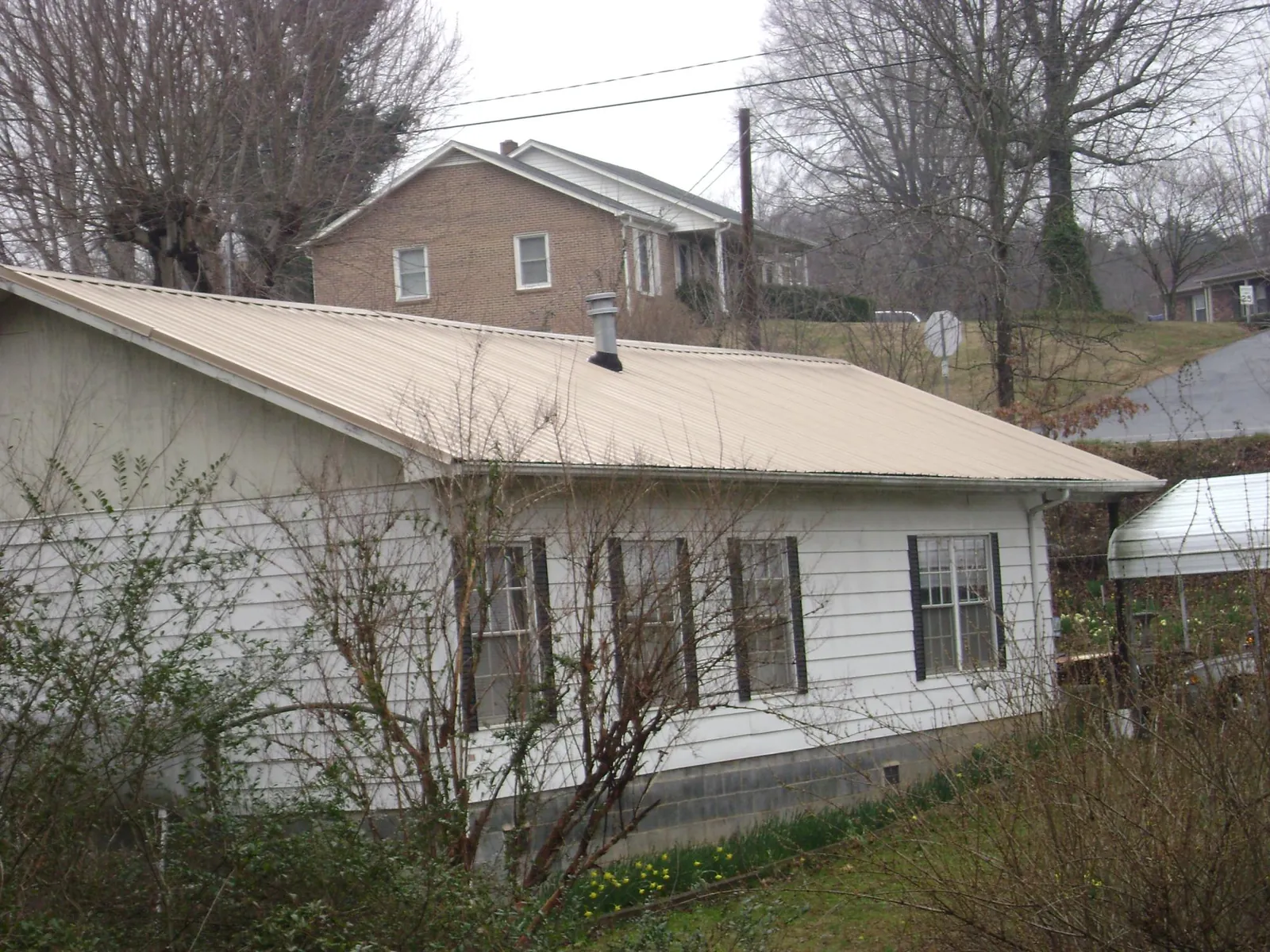 Tan metal roof on a white sided house set into a hillside — Commercial Roofing by Roofing Brothers in Hollidaysburg